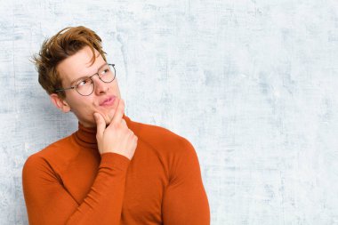 Genç kızıl saçlı adam düşünceli, meraklı ya da hayal kuruyor, hayal kuruyor ve grunge duvarına karşı uzayı kopyalamak istiyor.
