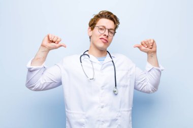 Genç kızıl kafalı doktor gururlu, kibirli ve kendinden emin, tatmin olmuş ve başarılı görünüyor, kendini mavi duvara gösteriyor.