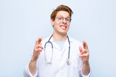 Genç kızıl saçlı doktor endişeyle dua ediyor ve mavi duvara karşı endişeli bir bakışla iyi şanslar diliyor.