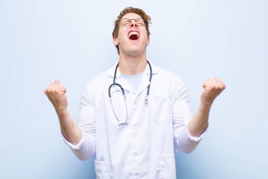 Genç kızıl saçlı doktor son derece mutlu ve şaşırmış görünüyor, başarıyı kutluyor, bağırıyor ve mavi duvara zıplıyor.