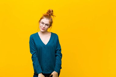 Genç kızıl saçlı kadın gururlu, kendinden emin, havalı, küstah ve küstah görünüyor, gülümsüyor, turuncu duvara karşı başarılı hissediyor.