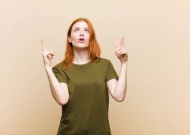 Genç kızıl saçlı güzel kadın şaşırmış, şaşırmış ve ağzı açık görünüyor, iki eliyle uzayı işaret ediyor.