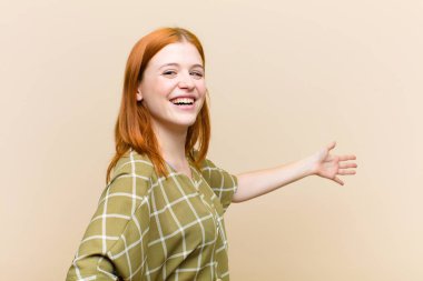 Genç kızıl saçlı güzel bir kadın mutlu ve neşeli hissediyor, gülümsüyor ve seni selamlıyor, dostça bir jestle içeri davet ediyor.