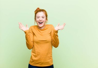 Genç, güzel, kızıl saçlı kadın mutlu, heyecanlı, şaşırmış ya da şok olmuş hissediyor. Yeşil duvara karşı inanılmaz bir şeye gülümsüyor ve şaşırıyor.