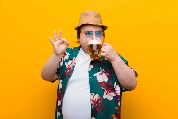young big size man with a pint of beer against flat wall