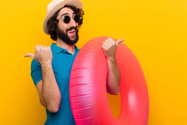 young crazy man smiling joyfully and looking happy, feeling carefree and positive with both thumbs up against orange wall