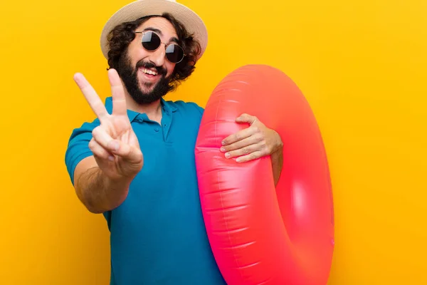 young crazy man smiling and looking happy, carefree and positive, gesturing victory or peace with one hand against orange wall