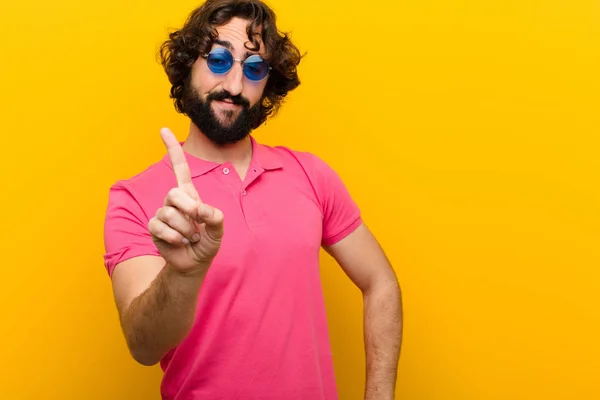 young crazy man smiling proudly and confidently making number one pose triumphantly, feeling like a leader against orange wall