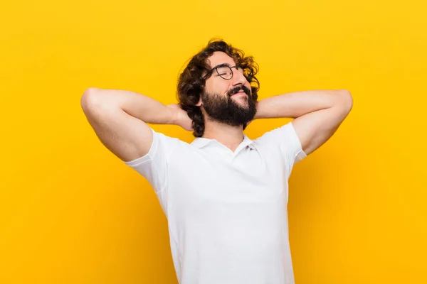 young crazy man smiling and feeling relaxed, satisfied and carefree, laughing positively and chilling against yellow wall