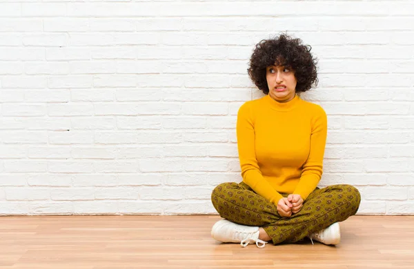 Genç güzel afro kadın endişeli, stresli, endişeli ve korkmuş görünüyor, panikliyor ve dişlerini sıkıyor yerde oturuyor.