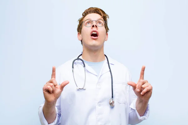 Young Red Head Doctor Feeling Awed Open Mouthed Pointing Upwards — Stock Photo, Image