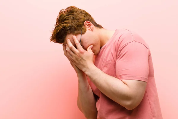 年轻的红头发男子双手捂住眼睛 一副悲伤 沮丧的绝望的表情 哭泣着 侧视着粉红的墙壁 — 图库照片