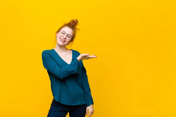 若い赤い頭の女性は陽気に笑って幸せを感じオレンジの壁に手の手のひらでコピースペースで概念を示す — ストック写真