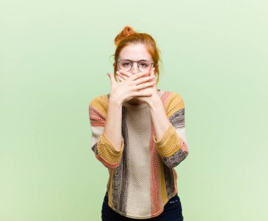 Genç, güzel, kızıl saçlı, elleri ile ağzını kapatan, şok olmuş, şaşırmış bir ifadeyle, sır saklayan ya da yeşil duvara karşı 