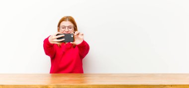 Genç kızıl saçlı güzel bir kadın ahşap bir masanın önünde cep telefonuyla.