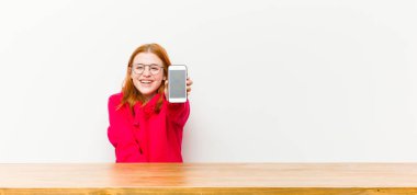 Genç kızıl saçlı güzel bir kadın ahşap bir masanın önünde cep telefonuyla.