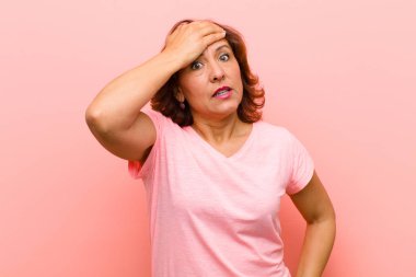 Orta yaşlı bir kadın unutulmuş bir süre için panikliyor, stresli hissediyor, pembe duvara karşı bir karmaşayı ya da hatayı örtbas etmek zorunda kalıyor.