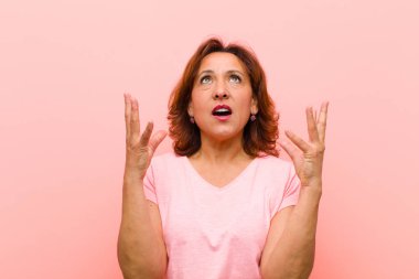 Orta yaşlı bir kadın öfkeyle bağırıyor, stresli hissediyor ve ellerini havaya kaldırıp neden pembe duvara yaslandığımı söylüyor.