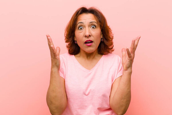 middle age woman looking shocked and astonished, with jaw dropped in surprise when realizing something unbelievable against pink wall