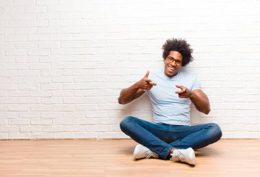 Genç siyah adam kendini mutlu, sakin, tatmin olmuş, rahat ve başarılı hissediyor, kameraya bakıyor, seni evde yerde otururken seçiyor.