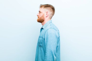 Profil görünümlü genç kızıl saçlı adam uzayı kopyalamaya çalışıyor, düşünüyor, hayal ediyor ya da hayal ediyor yumuşak mavi arka plana karşı.