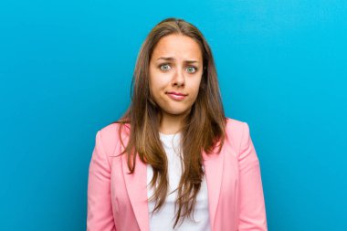 Genç bir kadın kendini şaşkın ve kuşkulu hissediyor, merak ediyor ya da mavi arka planda bir karar vermeye çalışıyor.