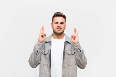 Genç İspanyol adam endişeyle dua ediyor ve gri arka planda endişeli bir bakışla iyi şanslar diliyor.