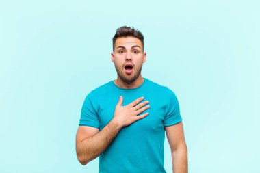 Genç İspanyol adam şok olmuş ve şaşırmış hissediyor, gülümsüyor, el ele tutuşuyor, mutlu ya da mavi arka plana karşı minnettarlık gösteriyor.