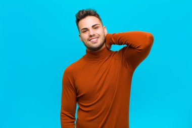 Genç İspanyol adam neşeli ve kendinden emin bir şekilde gülüyor mavi arka planda gülen, mutlu, dostane bir gülümsemeyle.