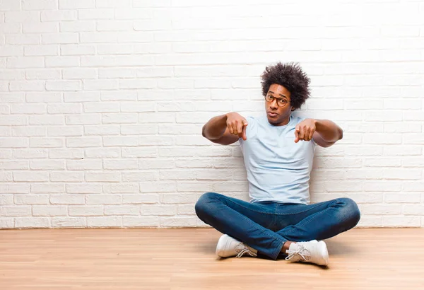 young black man pointing forward at camera with both fingers and angry expression, telling you to do your duty sitting on the floor at home