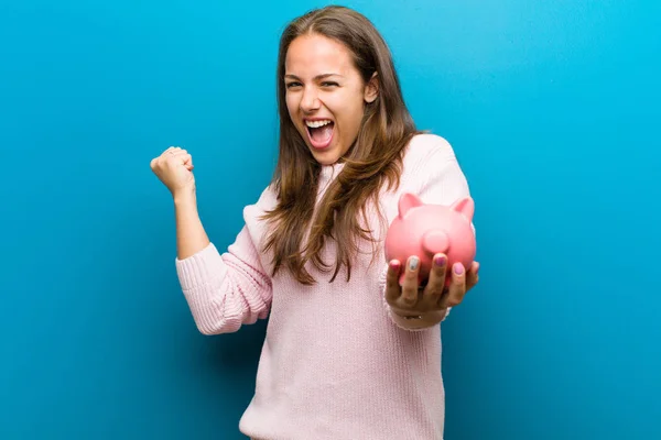 Jonge vrouw met een Piggy Bank tegen blauwe achtergrond — Stockfoto