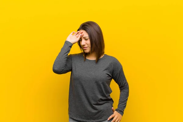 latin american woman looking stressed, tired and frustrated, drying sweat off forehead, feeling hopeless and exhausted isolated against yellow wall