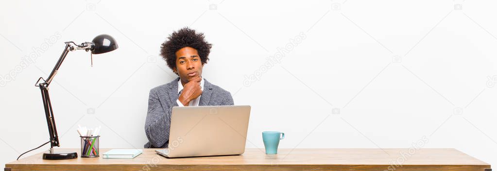 young black businessman looking serious, confused, uncertain and thoughtful, doubting among options or choices on a desk