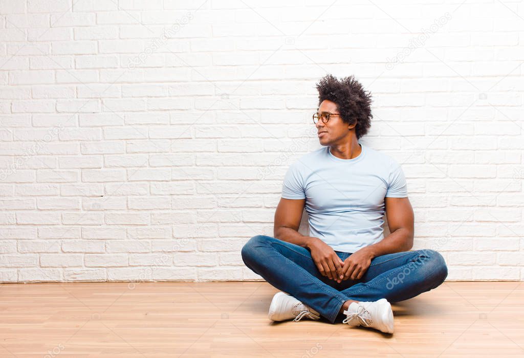 young black man on profile view looking to copy space ahead, thinking, imagining or daydreaming sitting on the floor at home