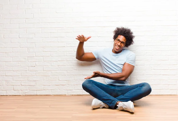 若い黒人男性は笑顔で 幸せを感じ 肯定的で満足し 家の床に座っているコピースペースにオブジェクトやコンセプトを保持または表示します — ストック写真