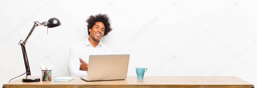 young black businessman laughing happily with arms crossed, with a relaxed, positive and satisfied pose on a desk