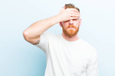 Genç kızıl saçlı adam gözlerini kapatıyor. Korkmuş ya da endişeli, merak ediyor ya da körü körüne mavi arka plana karşı bir sürpriz bekliyor.