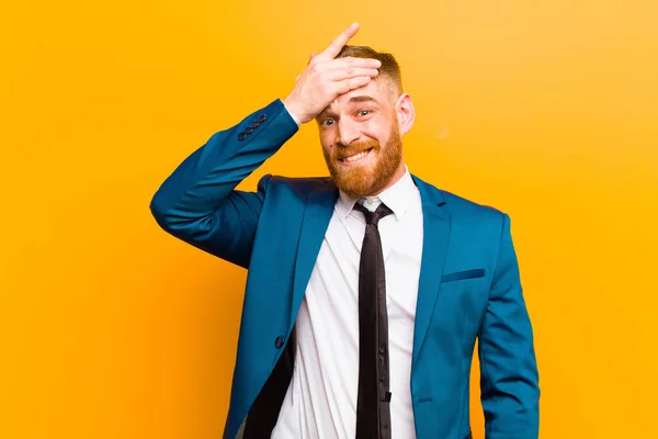 young red head businessman panicking over a forgotten deadline, feeling stressed, having to cover up a mess or mistake against orange background