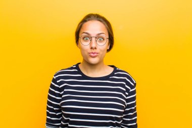 Genç, güzel bir kadın dudaklarını birbirine bastırıyor. Tatlı, eğlenceli, mutlu, sevimli bir yüz ifadesiyle. Turuncu arka plana öpücük yolluyor.