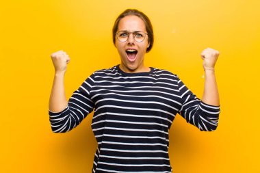 Genç ve güzel bir kadın sinirli bir ifadeyle ya da turuncu arka planda başarıyı kutlayan yumruklarla agresif bir şekilde bağırıyor.