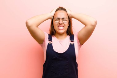 Genç bir kadın kendini stresli ve endişeli hissediyor. Depresyonda ve baş ağrısı yüzünden hayal kırıklığına uğramış. İki elini de pembe arka plana doğru kaldırıyor.