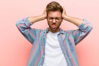 Genç adam kendini stresli ve hayal kırıklığına uğramış hissediyor, ellerinizi havaya kaldırıyor, yorgun, mutsuz ve pembe arka planda migreni var.