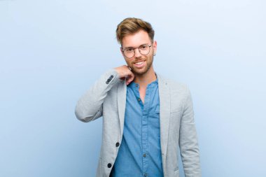 Genç işadamı neşeli ve kendinden emin bir şekilde gülüyor. Mavi arka planda gülen, mutlu, dostane bir gülümsemeyle.