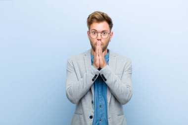 Genç işadamı endişeli, üzgün ve korkmuş hissediyor, elleriyle ağzını kapatıyor, endişeli görünüyor ve mavi arka planda berbat durumda.