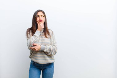 Genç, güzel bir kadın düşünüyor, kuşkulu ve şaşkın hissediyor, farklı seçenekleri var, beyaz duvara karşı hangi kararı vereceğimi merak ediyor.