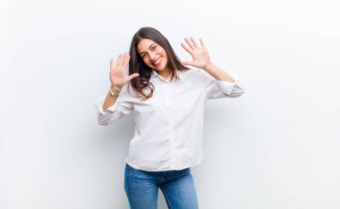 Genç ve güzel bir kadın gülümsüyor ve arkadaş canlısı görünüyor, onuncu veya onuncu numarayı gösteriyor, eli önde, beyaz duvara karşı geriye doğru sayıyor.