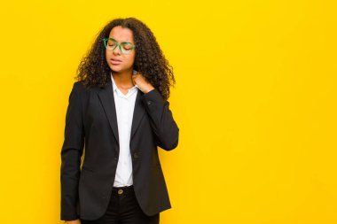 Zenci iş kadını stresli, endişeli, yorgun ve hayal kırıklığına uğramış, tişörtünü çekmiş, turuncu duvara karşı sorunlu görünüyor.