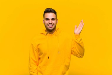 young hispanic man feeling happy, surprised and cheerful, smiling with positive attitude, realizing a solution or idea against orange wall clipart