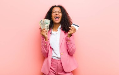 Pembe duvar arkasında dolar banknotları olan genç siyah güzel bir kadın.