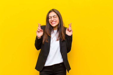 Genç, güzel bir kadın gülümsüyor ve endişeyle iki parmağını çapraz yapıyor. Endişeli ve turuncu duvara karşı iyi şanslar diliyor.